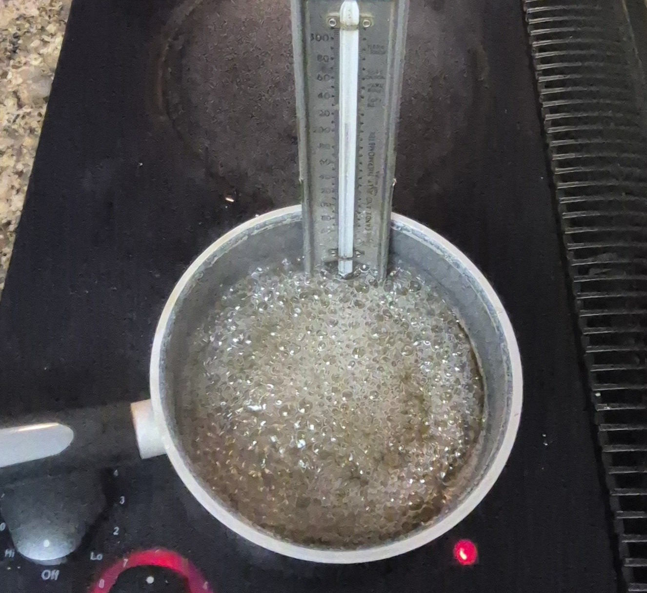 sugar and water on the stove with a candy thermometer